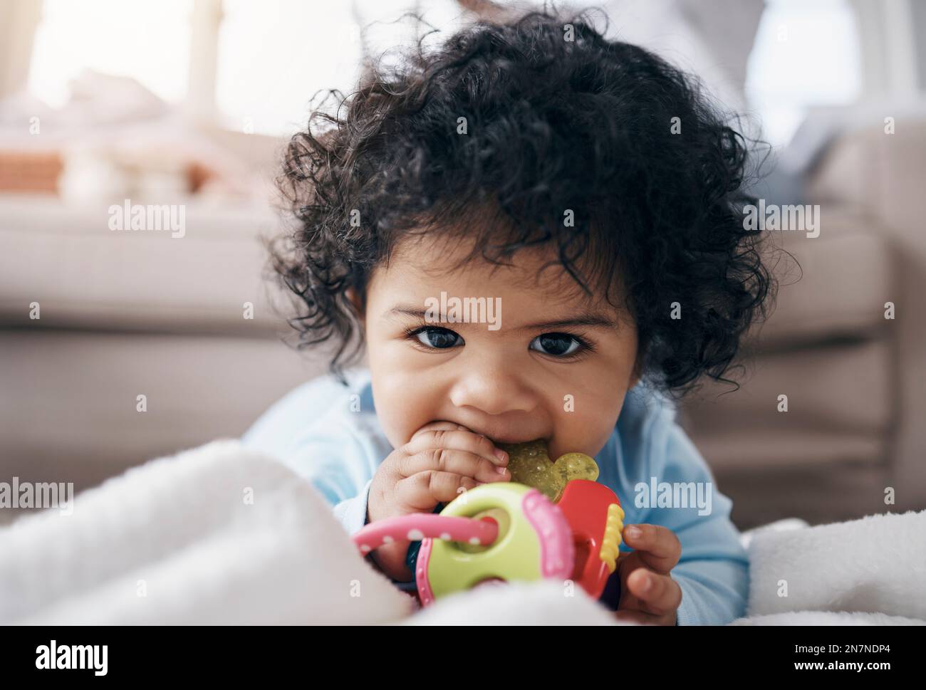 Can you tell Im teething. an adorable little girl lying on the floor in the living room and playing with a toy. Stock Photo