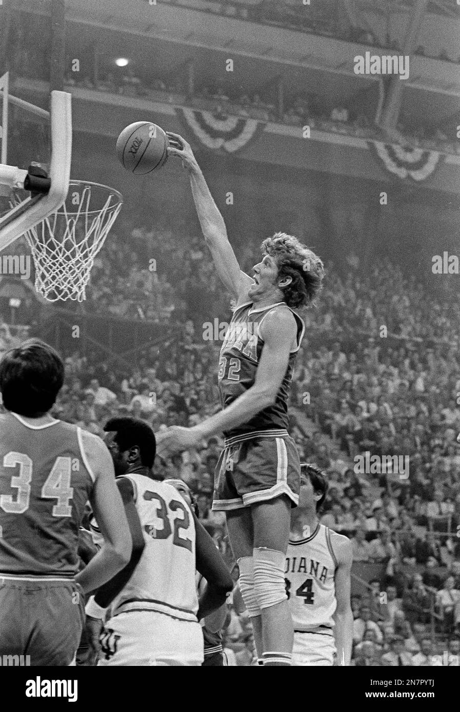FILE - In this March 26, 1973, file photo, UCLA's Bill Walton leaps high to dunk against Indiana during a national semifinal game at the Final Four of the NCAA college basketball tournament at St. Louis, Mo. In left foreground is teammate Dave Meyers, left, and Indiana center Steve Downing. UCLA won 70-59. (AP Photo/File) Stock Photo