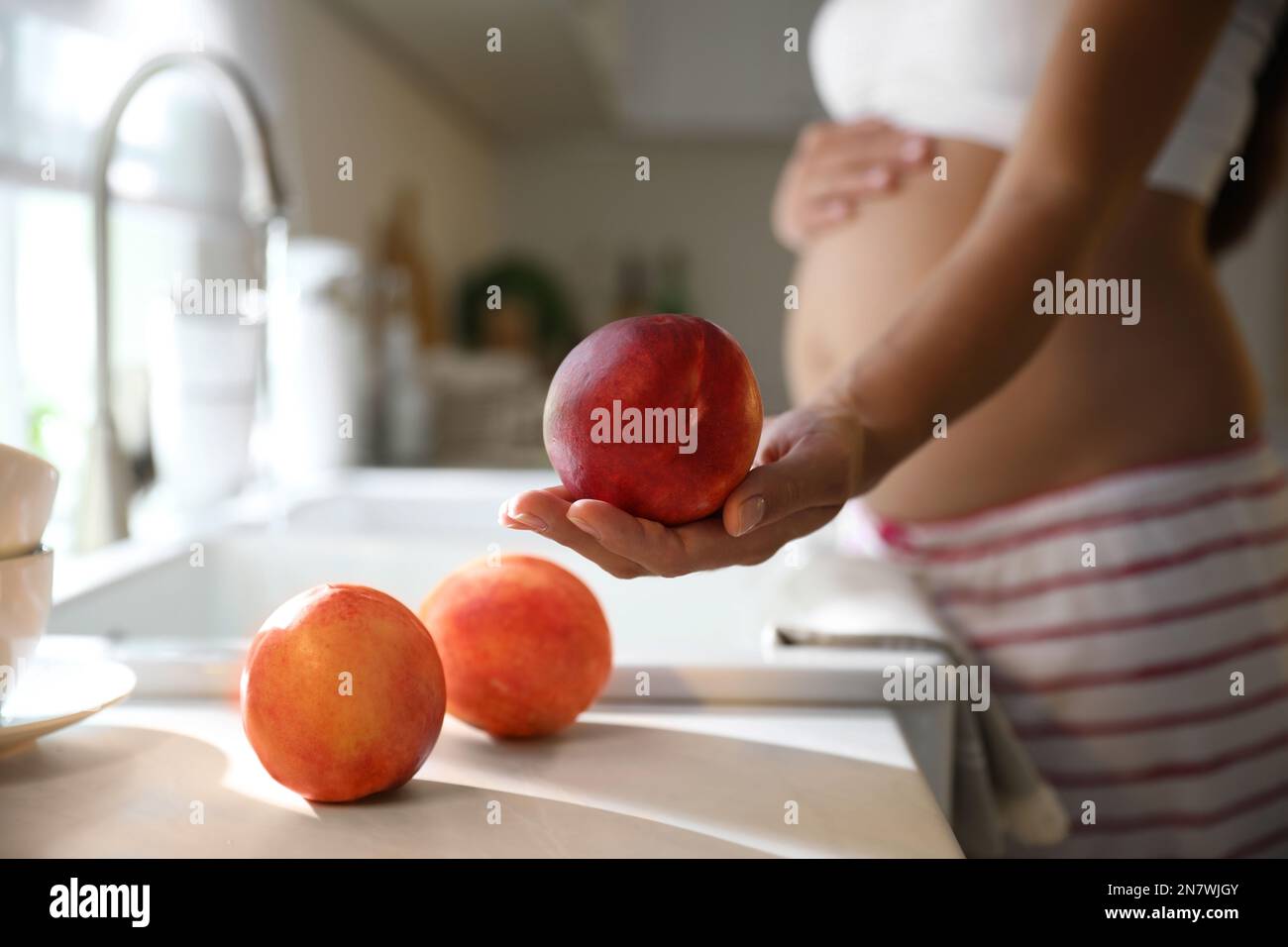 Young pregnant woman washing fresh sweet peaches in kitchen, closeup. Taking care of baby health