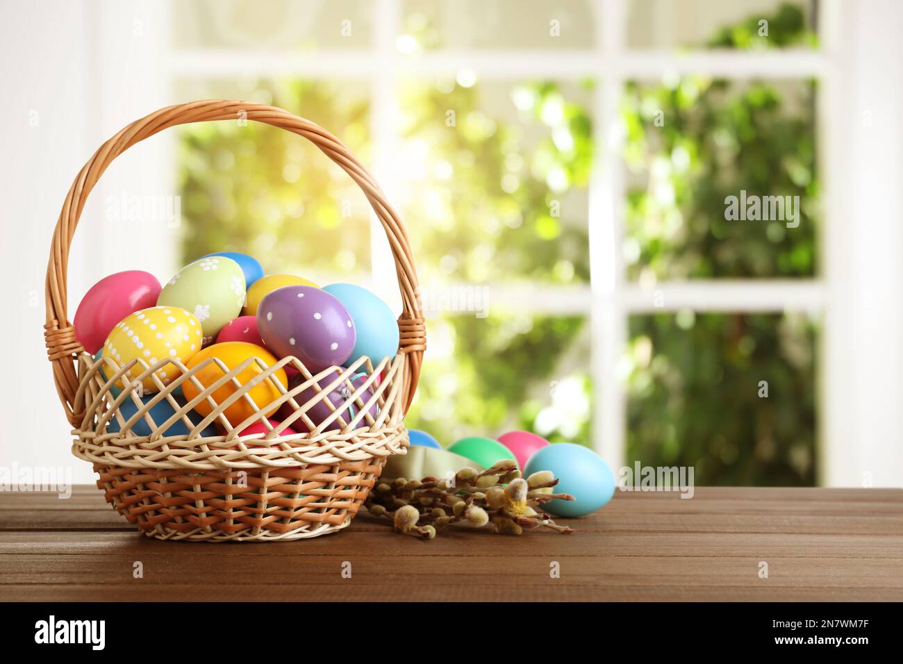 Colorful Easter eggs in wicker basket and willow branches on wooden ...