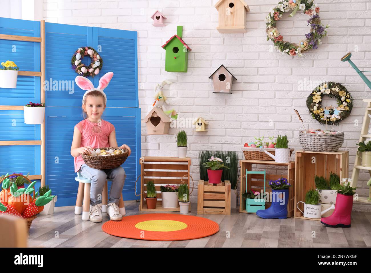 Adorable little girl with bunny ears and basket full of dyed eggs in Easter photo zone Stock