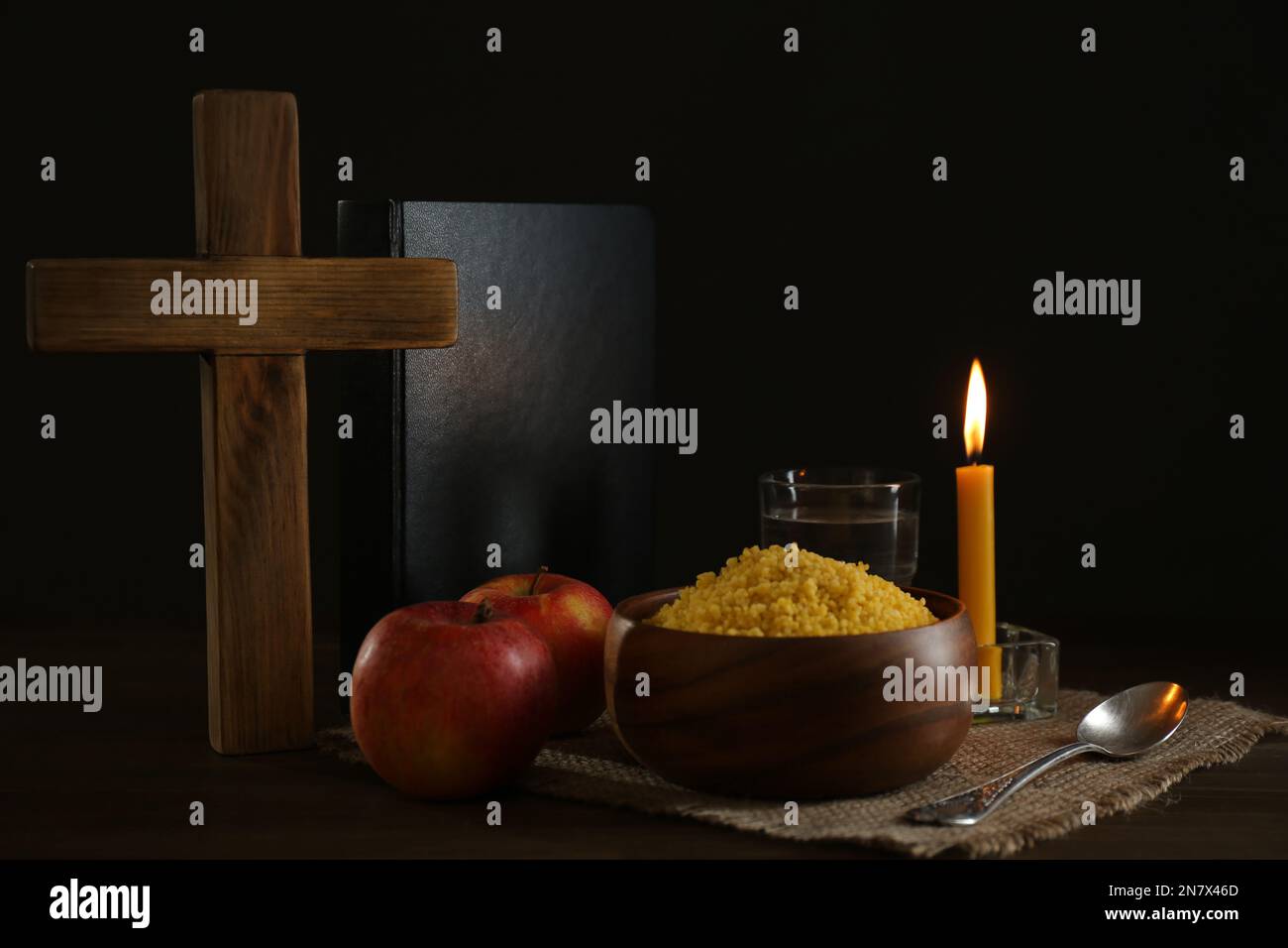 Millet, apple, water, burning candle, Bible and cross on wooden table