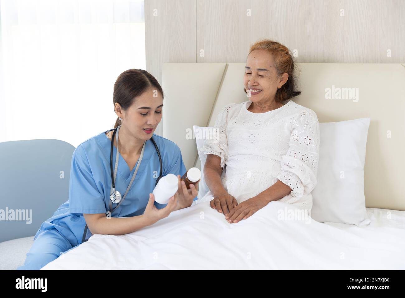 Nurse take care patient elderly senior asian woman present drug use to patients recovery on bed at home Stock Photo