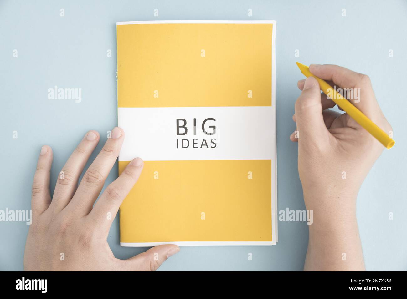 close up person holding yellow crayon with big idea book blue background Stock Photo