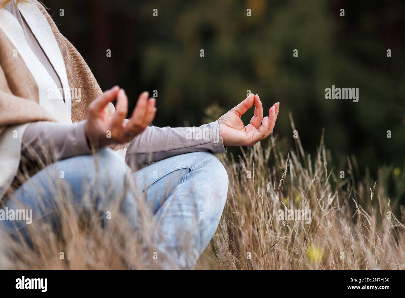 Woman practicing yoga exercise in lotus position. Meditation outdoors. Selective focus on hand Stock Photo