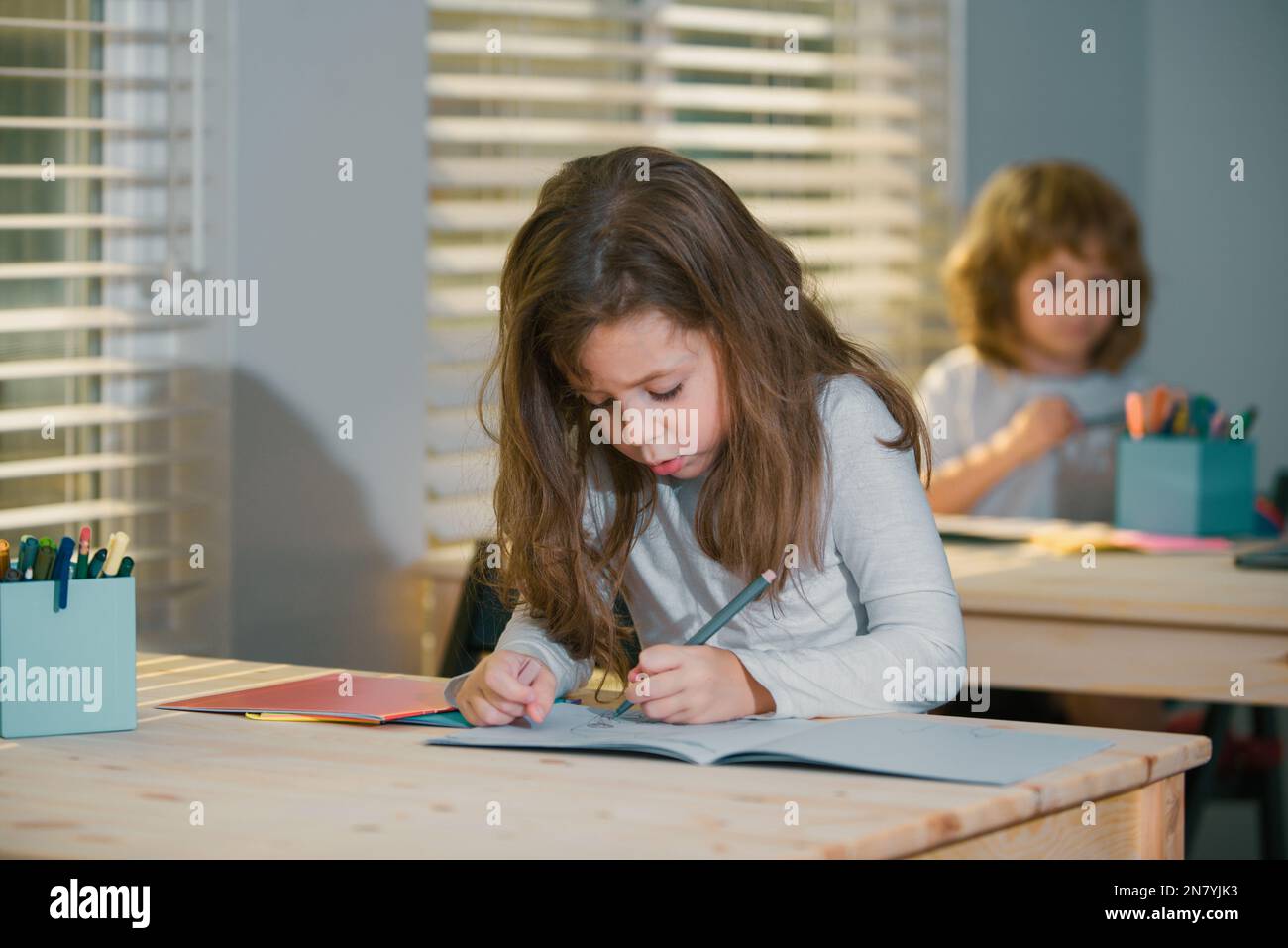 Portrait of cute girl sitting at desk in school classroom. Pupil ...