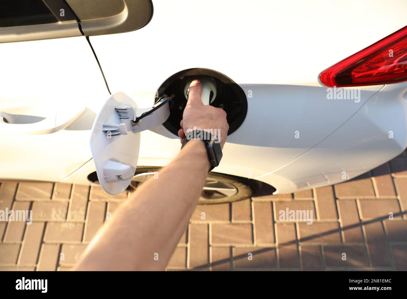 Man inserting plug into electric car socket at charging station, above