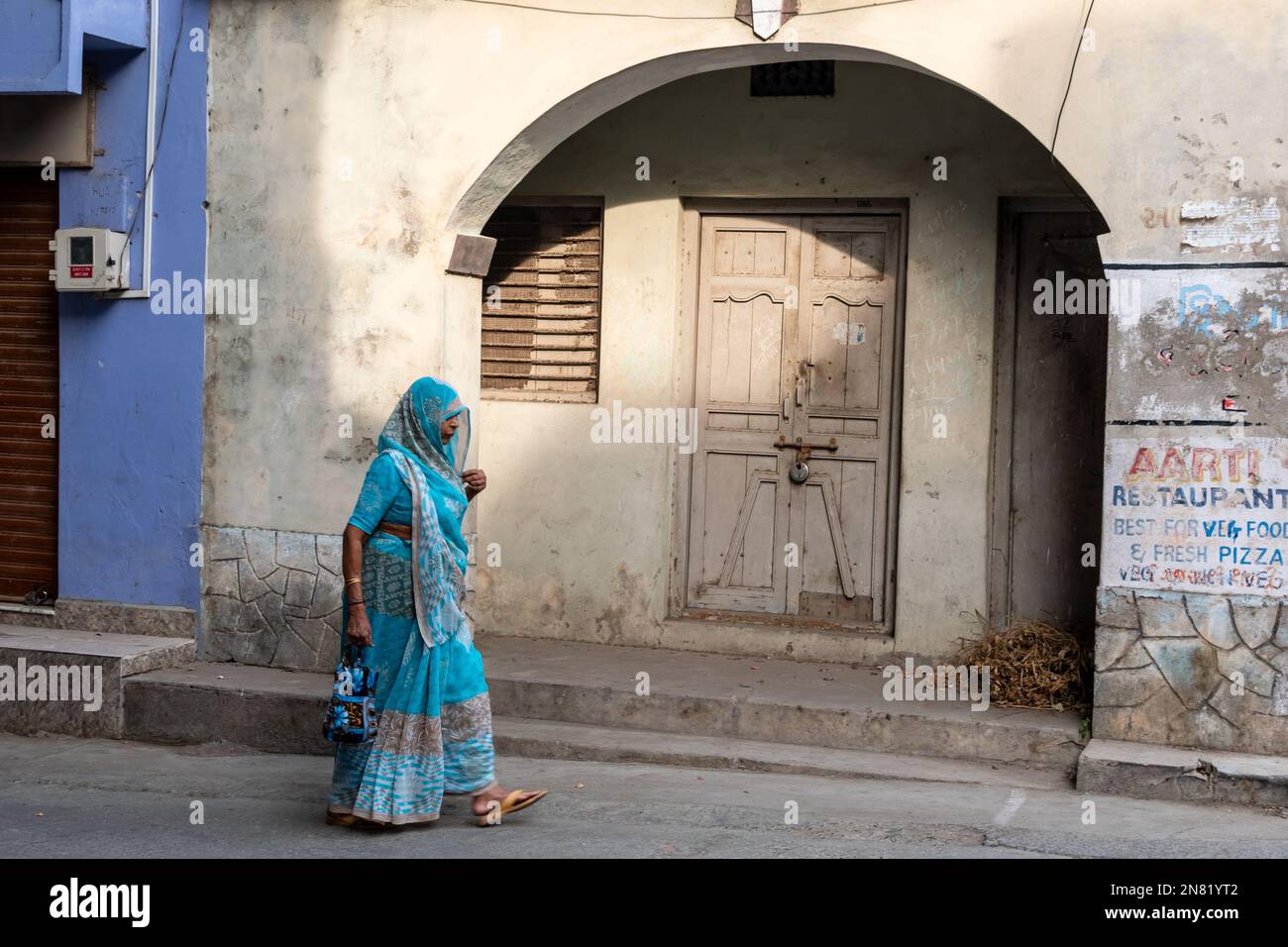 Diu, India - December 2018: An Indian woman wearing a bright blue sari walking past a vintage arched doorway in the island town of Diu. Stock Photo