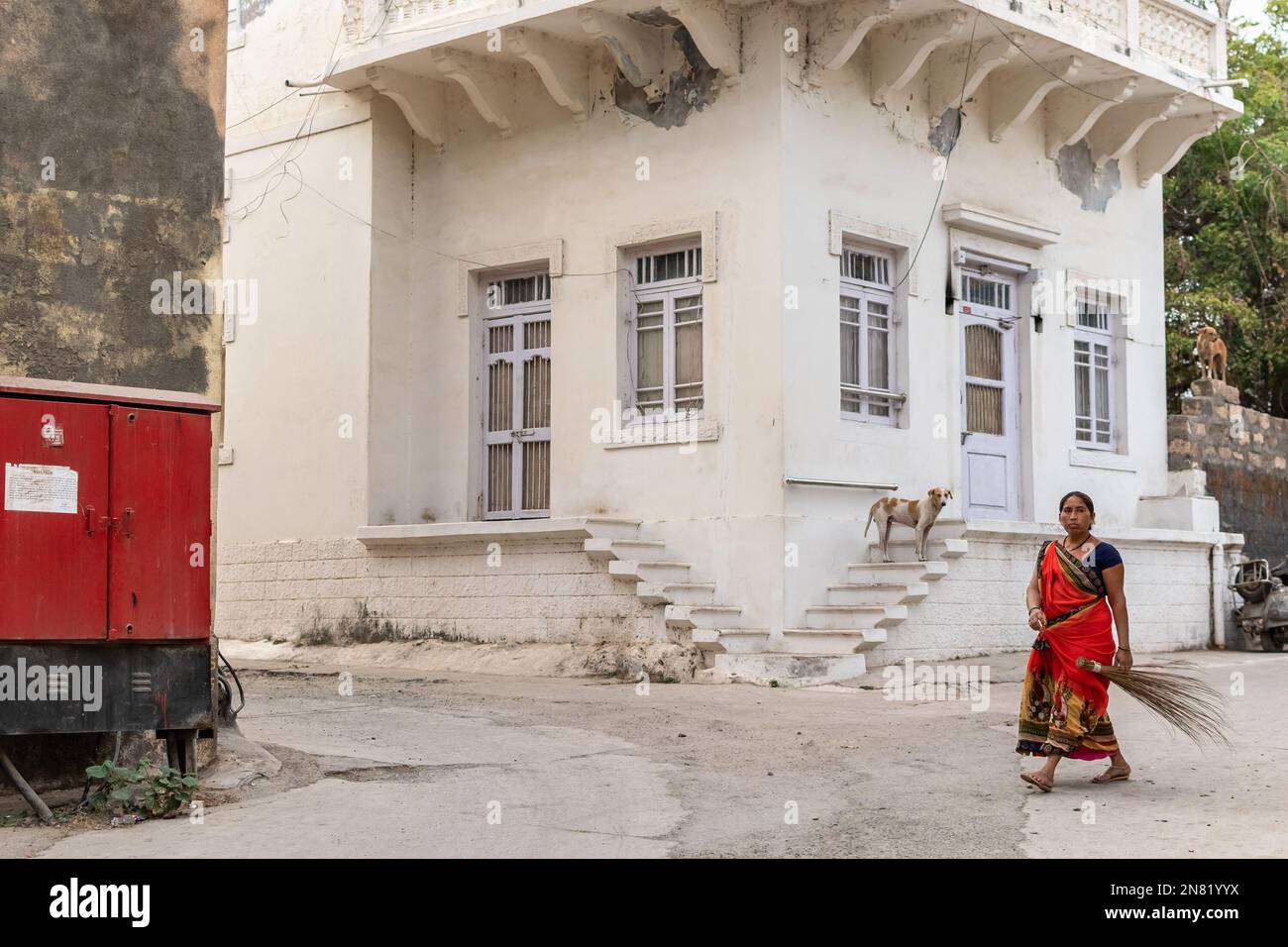 Diu, India - December 2018: An Indian women wearing a red sari walking with a broom stick past an old Portuguese era house in the island town of Diu. Stock Photo