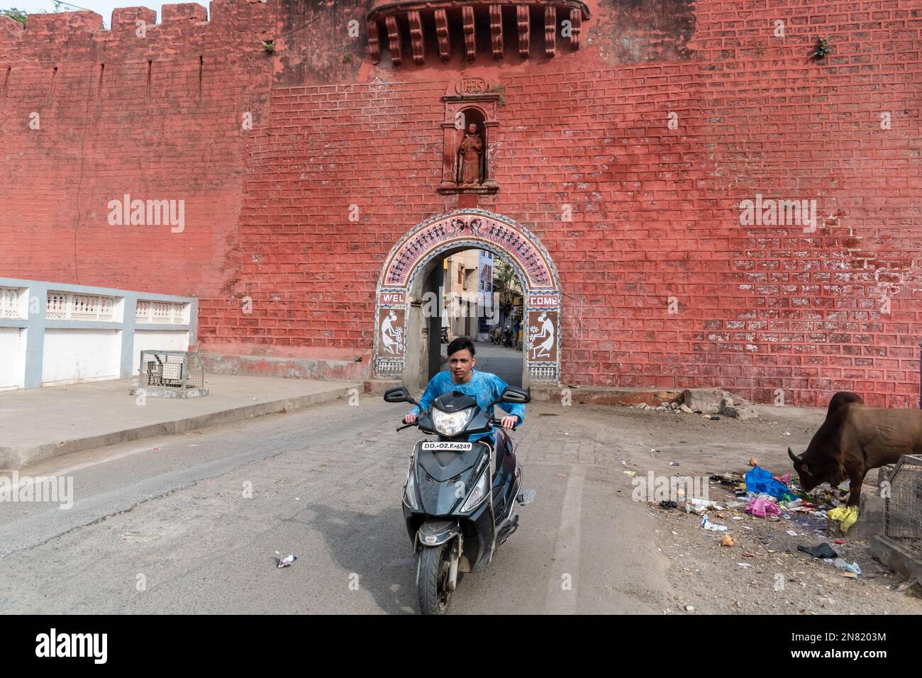 Diu, India - December 2018: A man riding a bike past the red walls of the Portuguese era Zampa gateway in Diu Island. Stock Photo