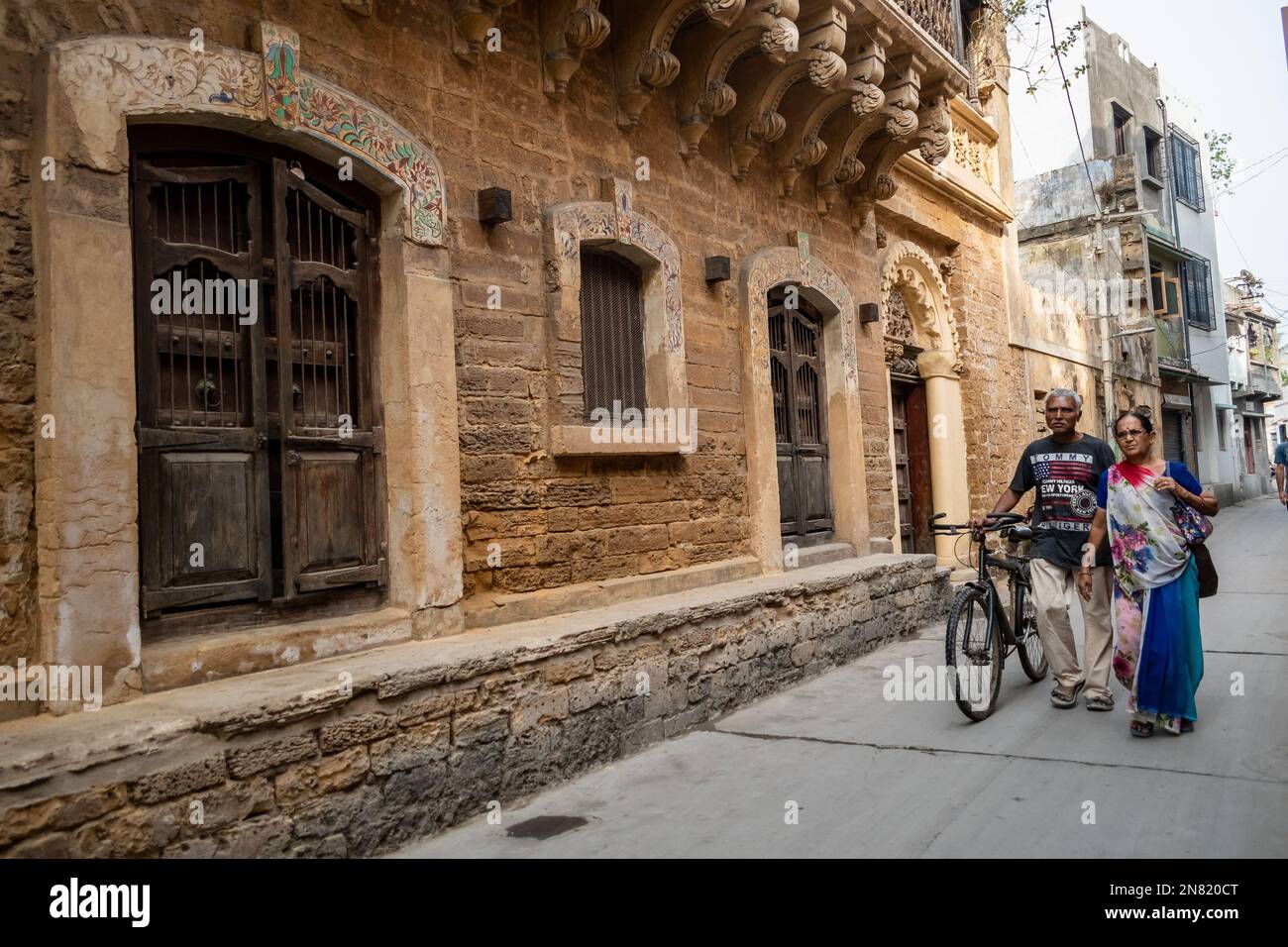 Diu, India - December 2018: An old man and a woman walking with a bicycle in a narrow street lined with old Portuguese era houses in the town of Diu. Stock Photo