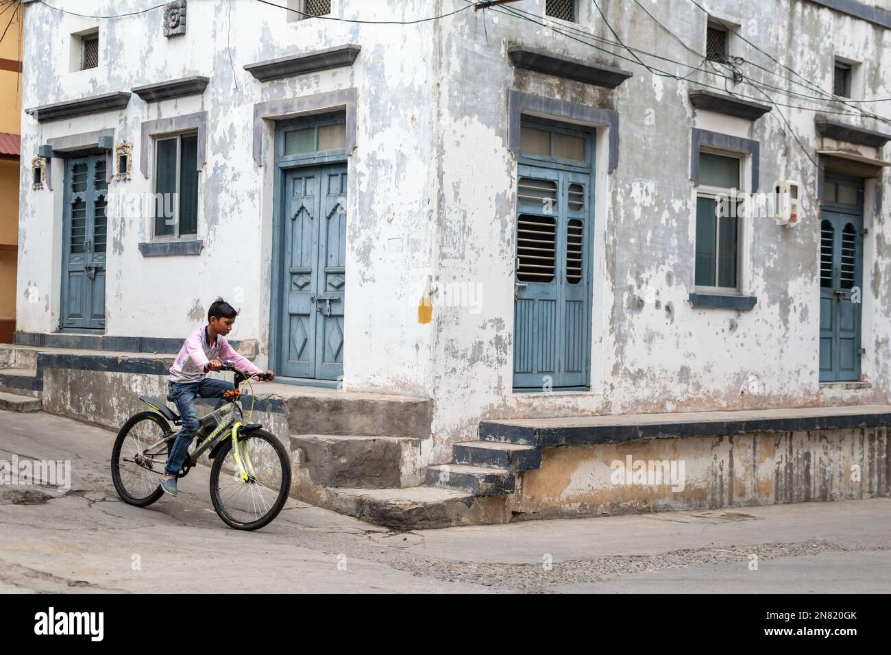 Diu, India - December 2018: A young boy riding a bicycle on a street with old Portuguese era houses in the island town of Diu. Stock Photo