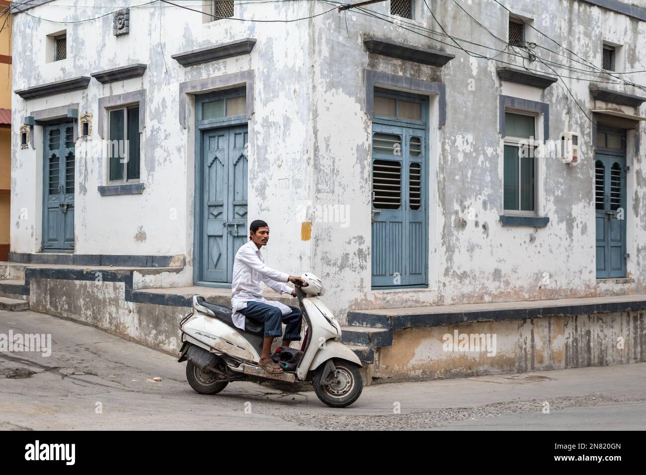 Diu, India - December 2018: A man riding a scooter bike on a street with old Portuguese era houses in the island town of Diu. Stock Photo