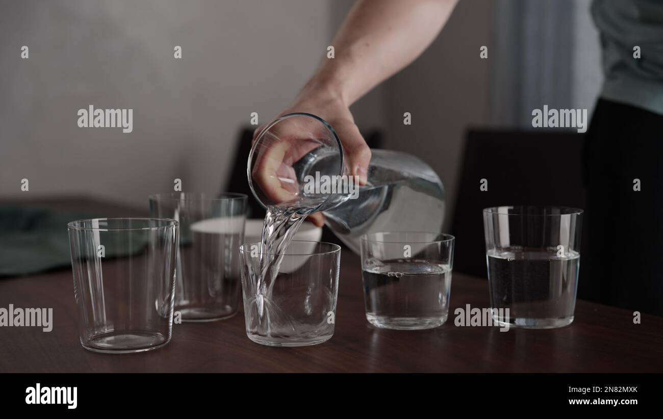 Man pour water into glasses from carafe on walnut table, wide photo ...