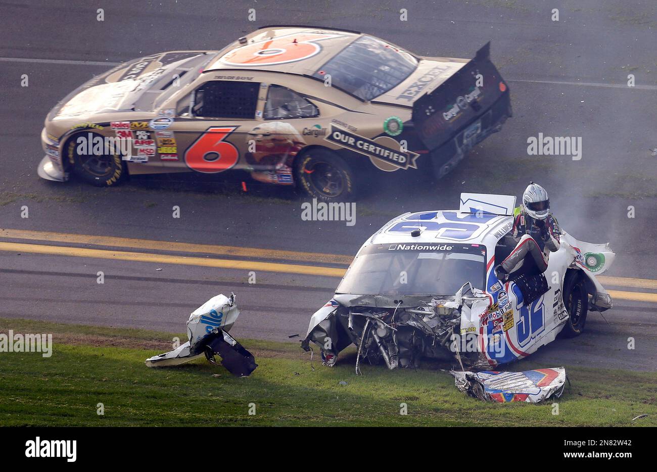 Driver Kyle Larson climbs out of his car as Trevor Bayne (7) rolls past after a crash at the conclusion of the NASCAR Nationwide Series auto race Saturday, Feb