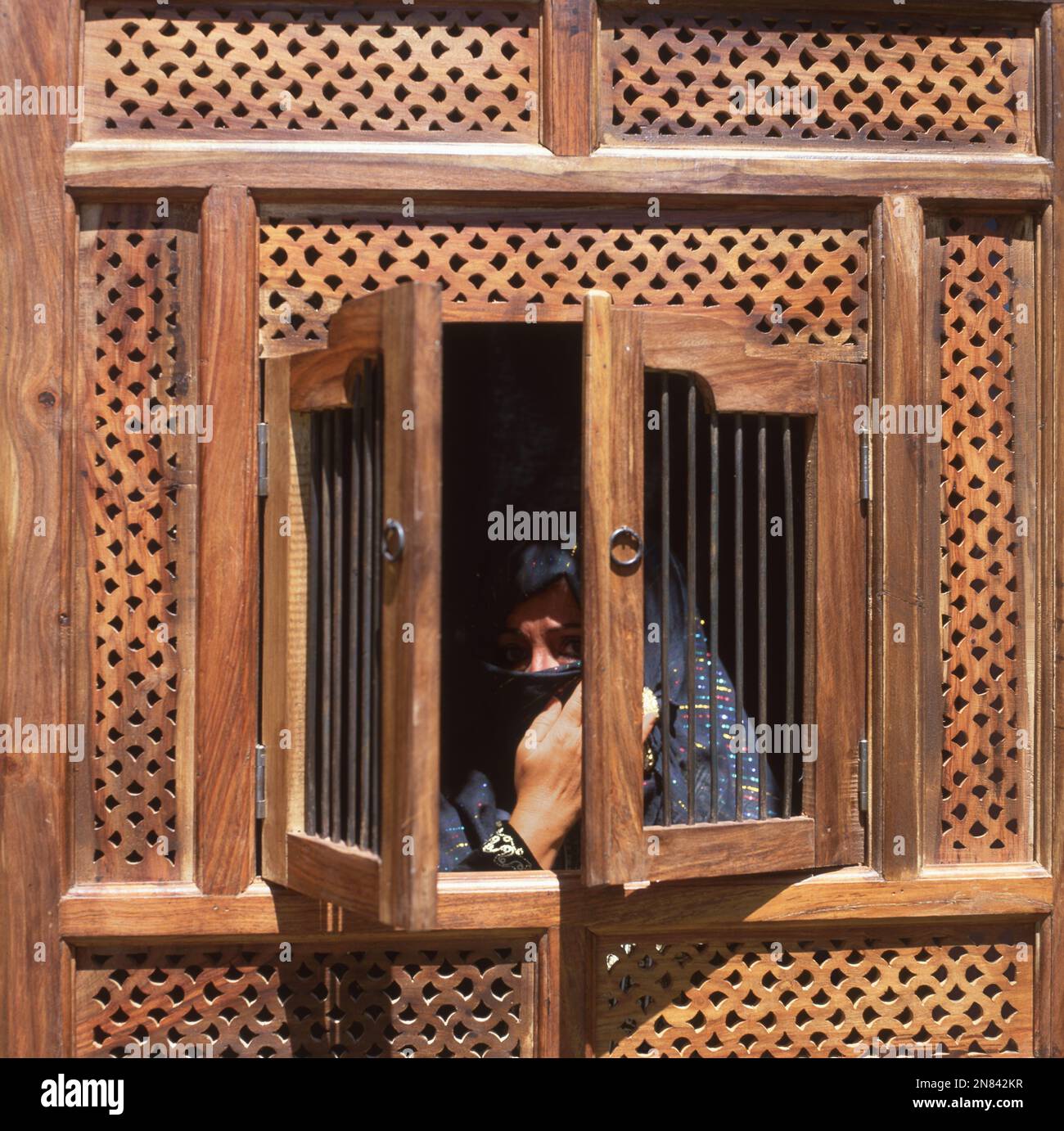 Frau hinter Holzfenster, Gesicht mit schwarzem Schleier verh��llt * woman behind a wooden window, holding her veil with her hand Stock Photo