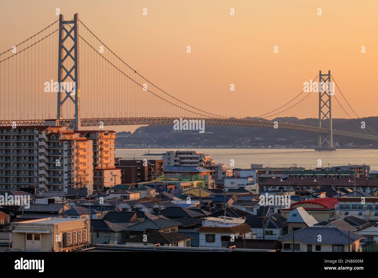 Orange sunset glow in sky over suspension bridge and dense small town ...