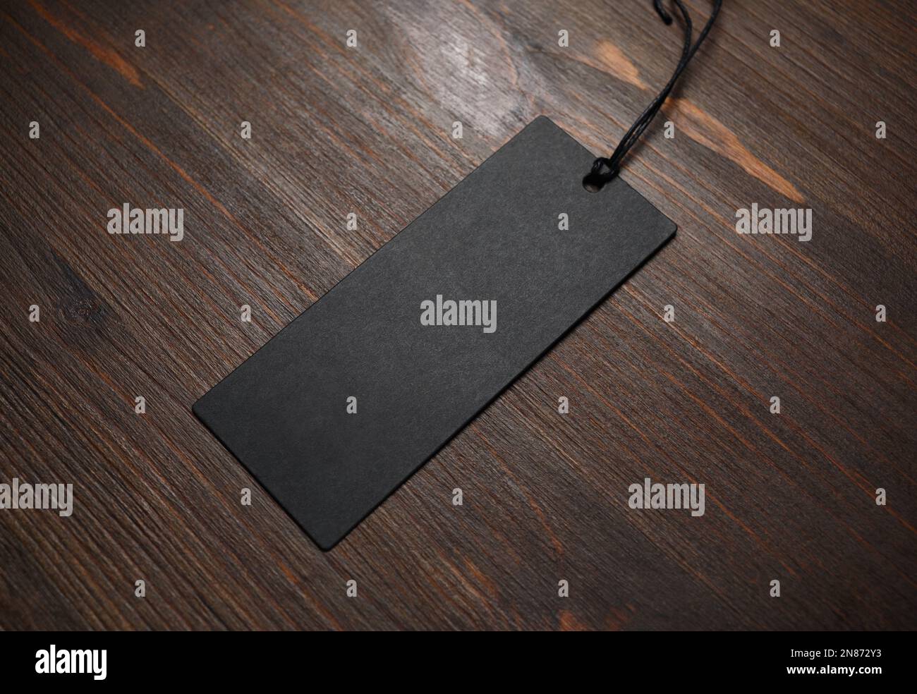 Blank black tag label with cord on wood table background. Mockup for