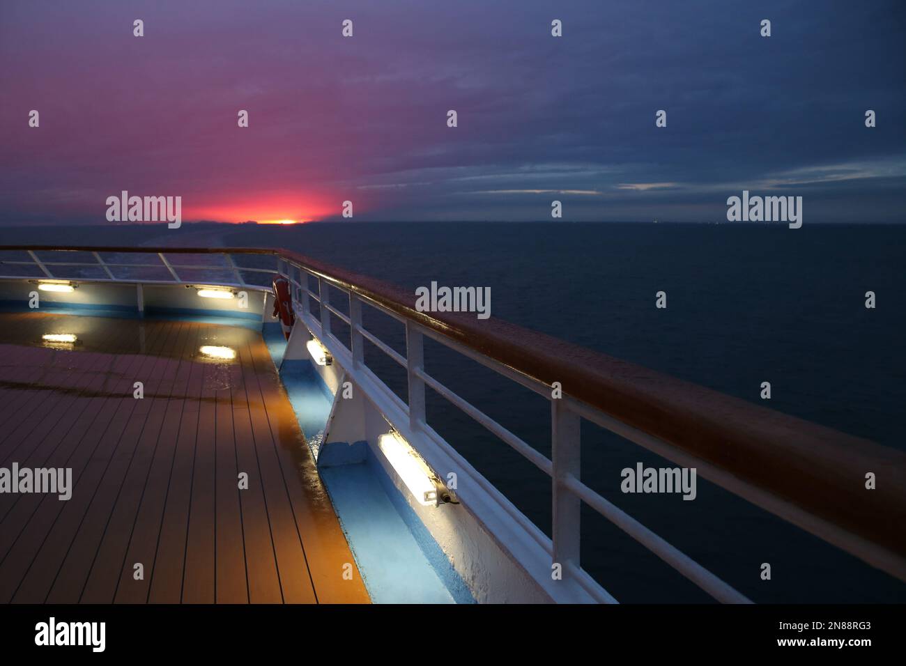 Beautiful final moments of the sunset with pink clouds over a cruise ship deck; a relaxing way to travel, sailing across the calm ocean. Stock Photo