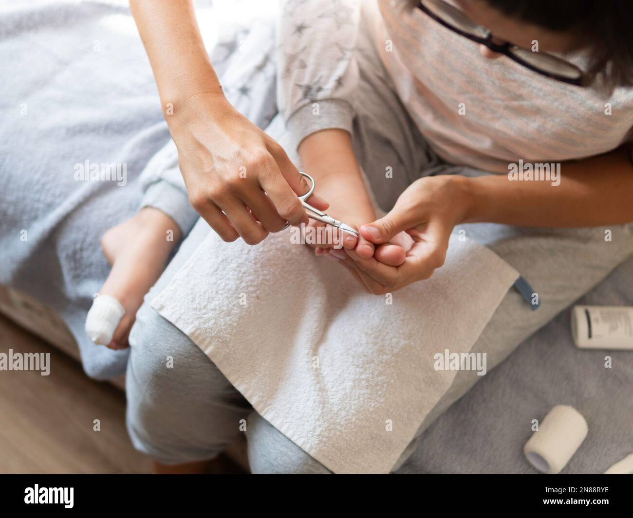Mother bandages her child's big toe and cuts nails on other foot. Close