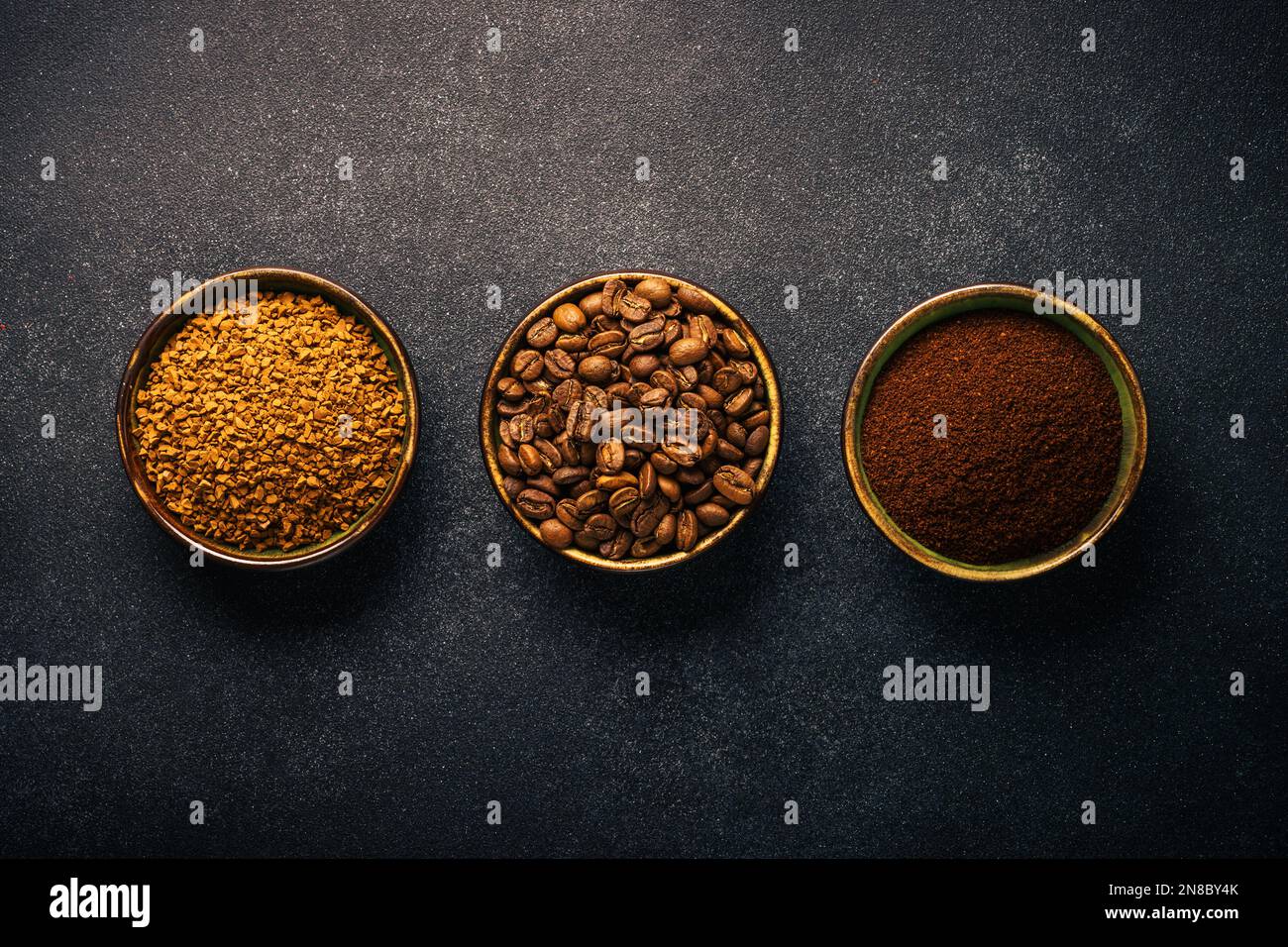 Roasted coffee beans, ground coffee and instant coffee in bowls at dark