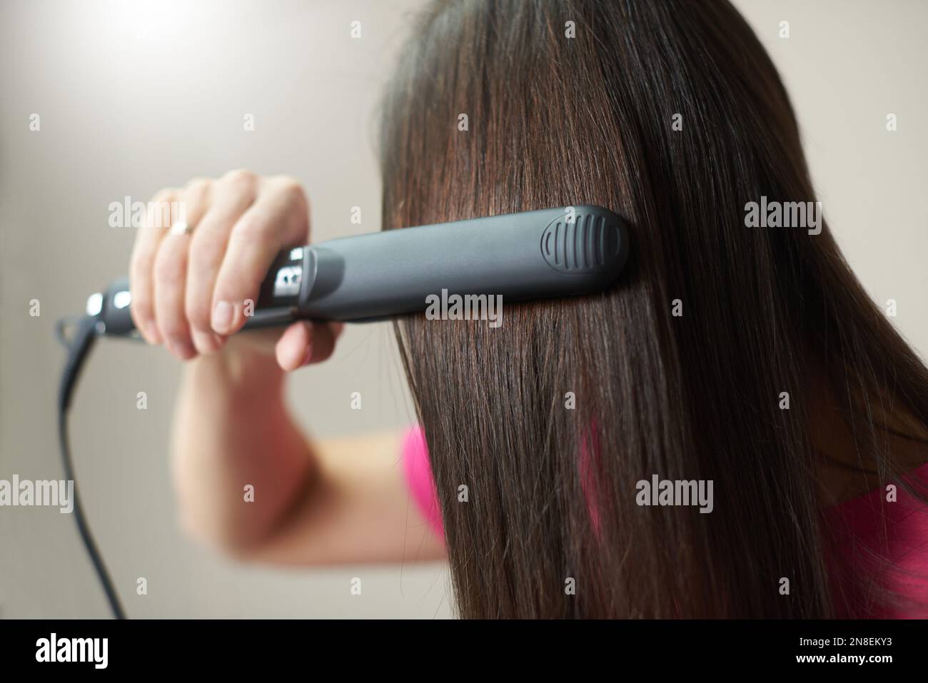 Brunette woman straightens her hair using an iron hair straightener. Stock Photo
