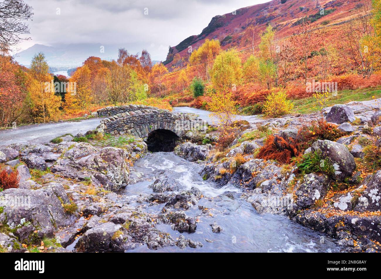 Steely greys with burnt autumn hues set the scene at the picturesque location of Ashness Bridge crossing Barrow Beck, Lake District National Park, UK Stock Photo
