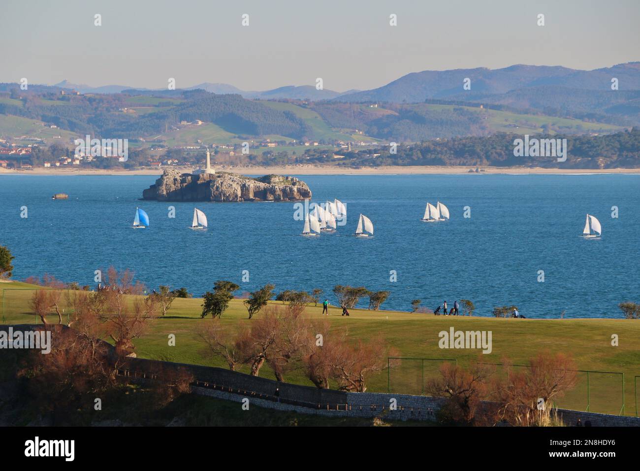 Landscape view across Matalenas Golf Course with a sailing competition underway and the Mouro Island and lighthouse Santander Cantabria Spain Stock Photo