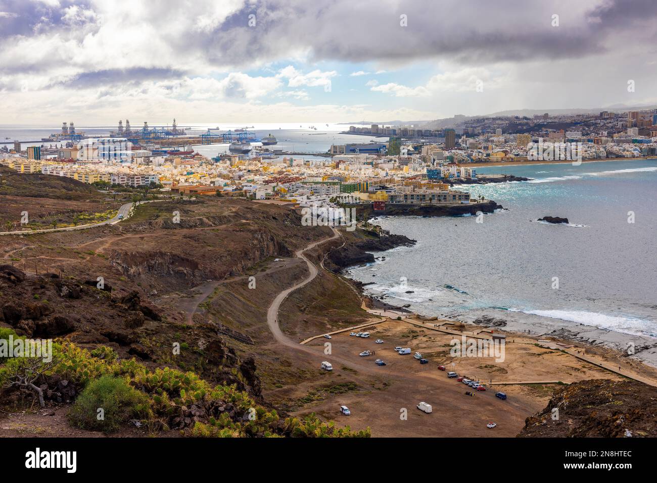 Las Palomas panorama with ships in the harbour from nearby hill on cloudy day. Ocean waves hitting the rocks on the beach. Stock Photo