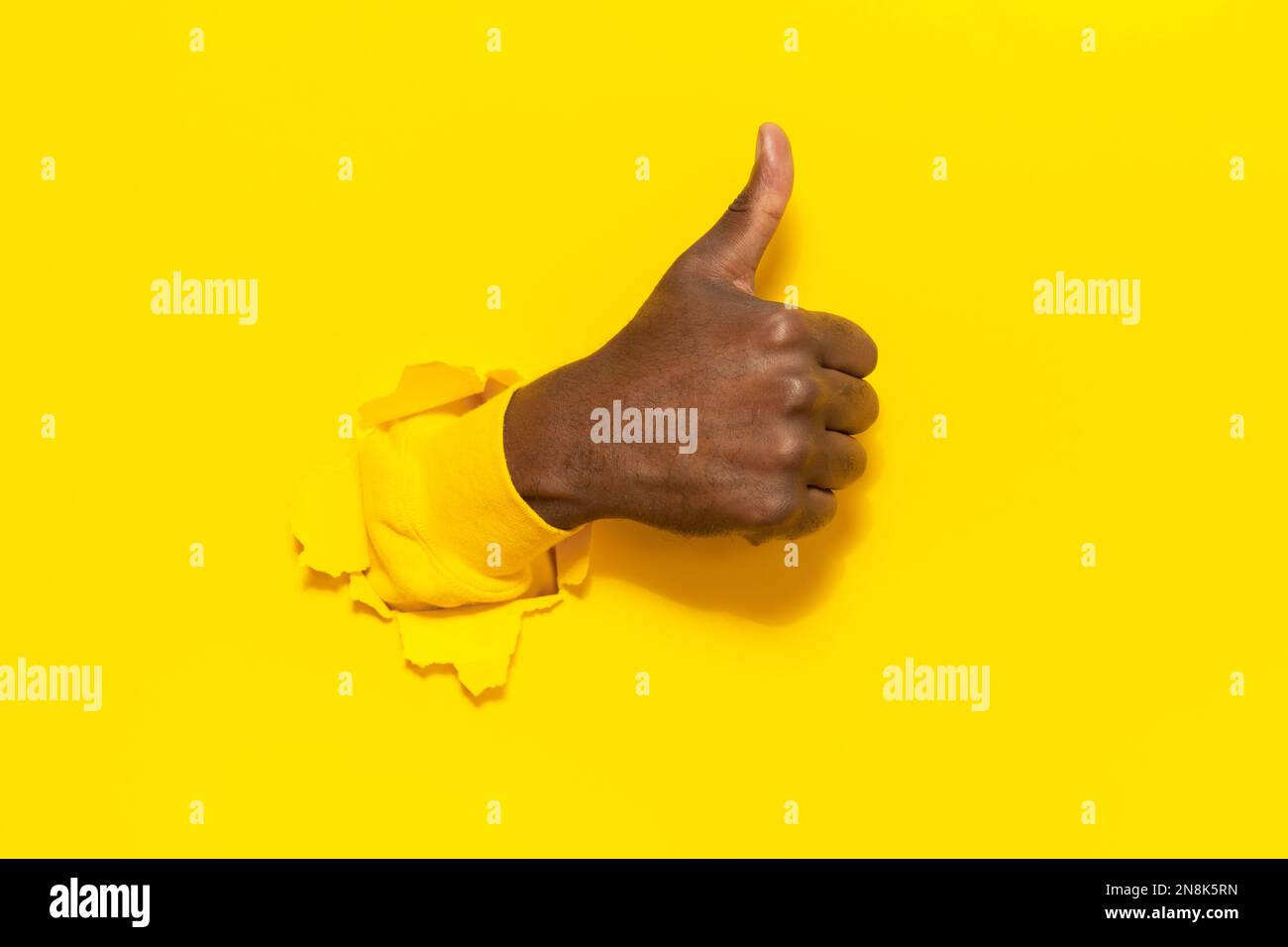 Black male gesturing thumb up, showing approval sign through hole in ...