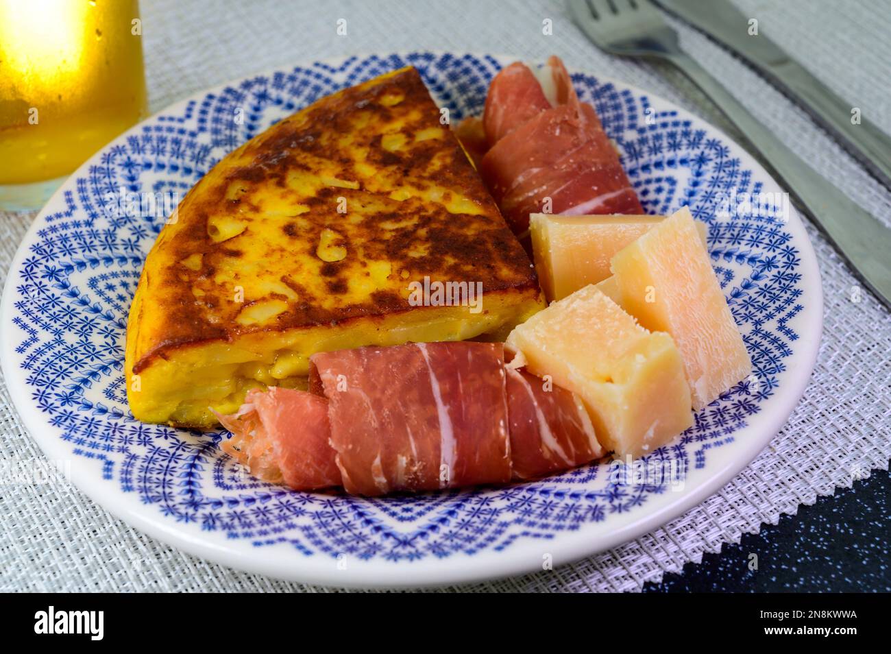 Spanish food, portion of potato omelette tortilla de patatas with onion served with cheese and jamon in cafe Stock Photo