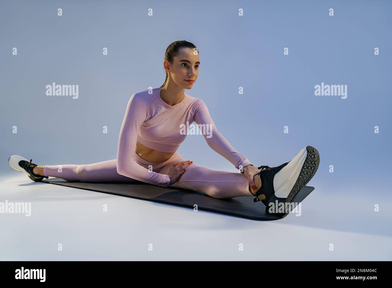 Sporty woman doing stretching exercises on yoga mat on studio ...