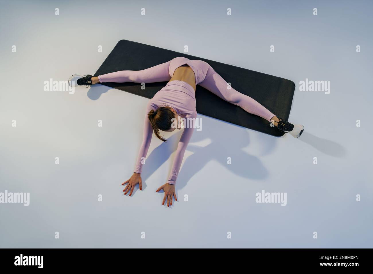 Flexible woman doing stretching exercises on yoga mat on studio ...