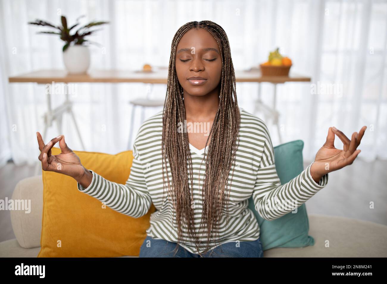 Relaxed young black woman meditating on sofa at home Stock Photo - Alamy