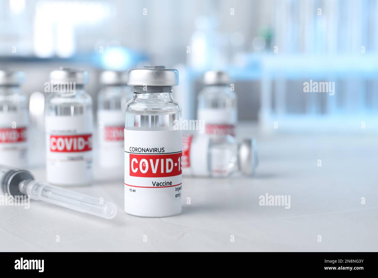 Glass vials with COVID-19 vaccine and syringe on light table. Space for ...