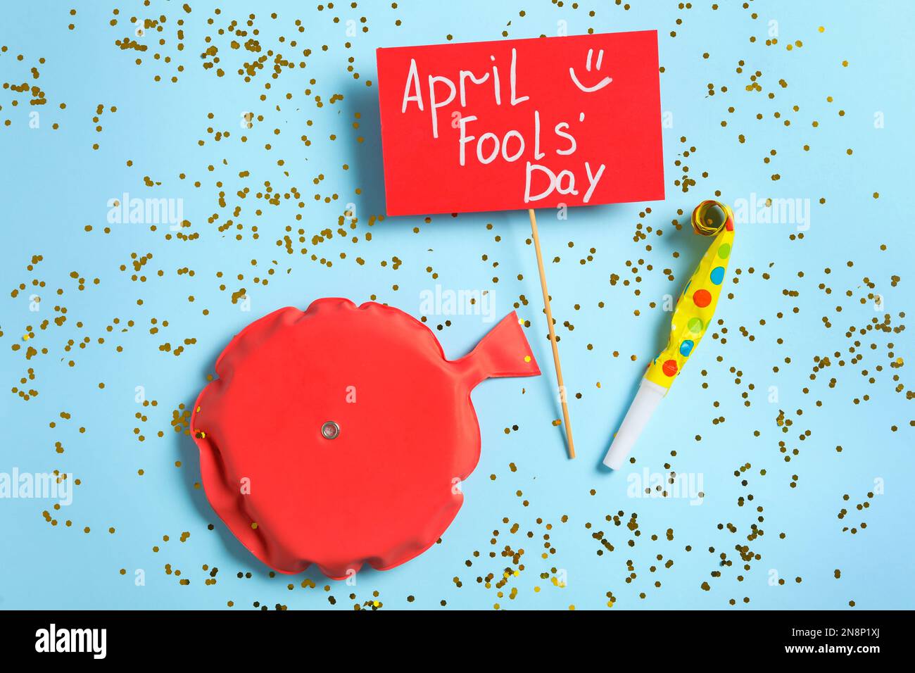 Sign with phrase April Fools' Day, whoopee cushion and party blower on light blue background, flat lay Stock Photo