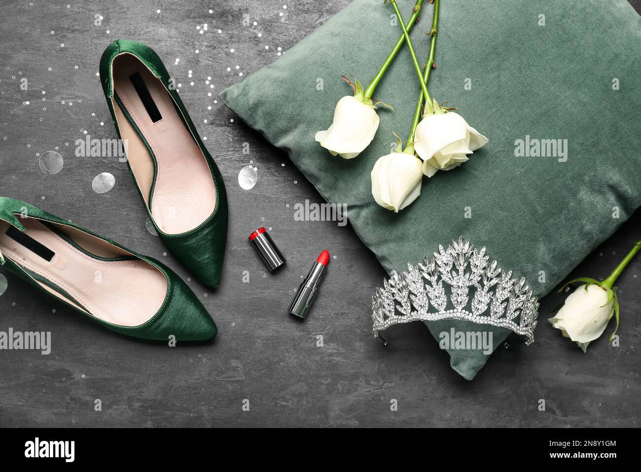 Beautiful tiara, pillow, roses, lipstick and heels on dark background