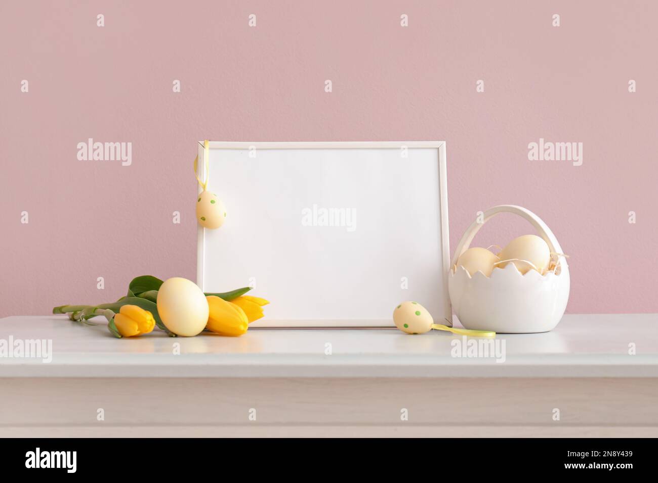 Blank frame, basket with painted easter eggs and yellow tulip flowers ...