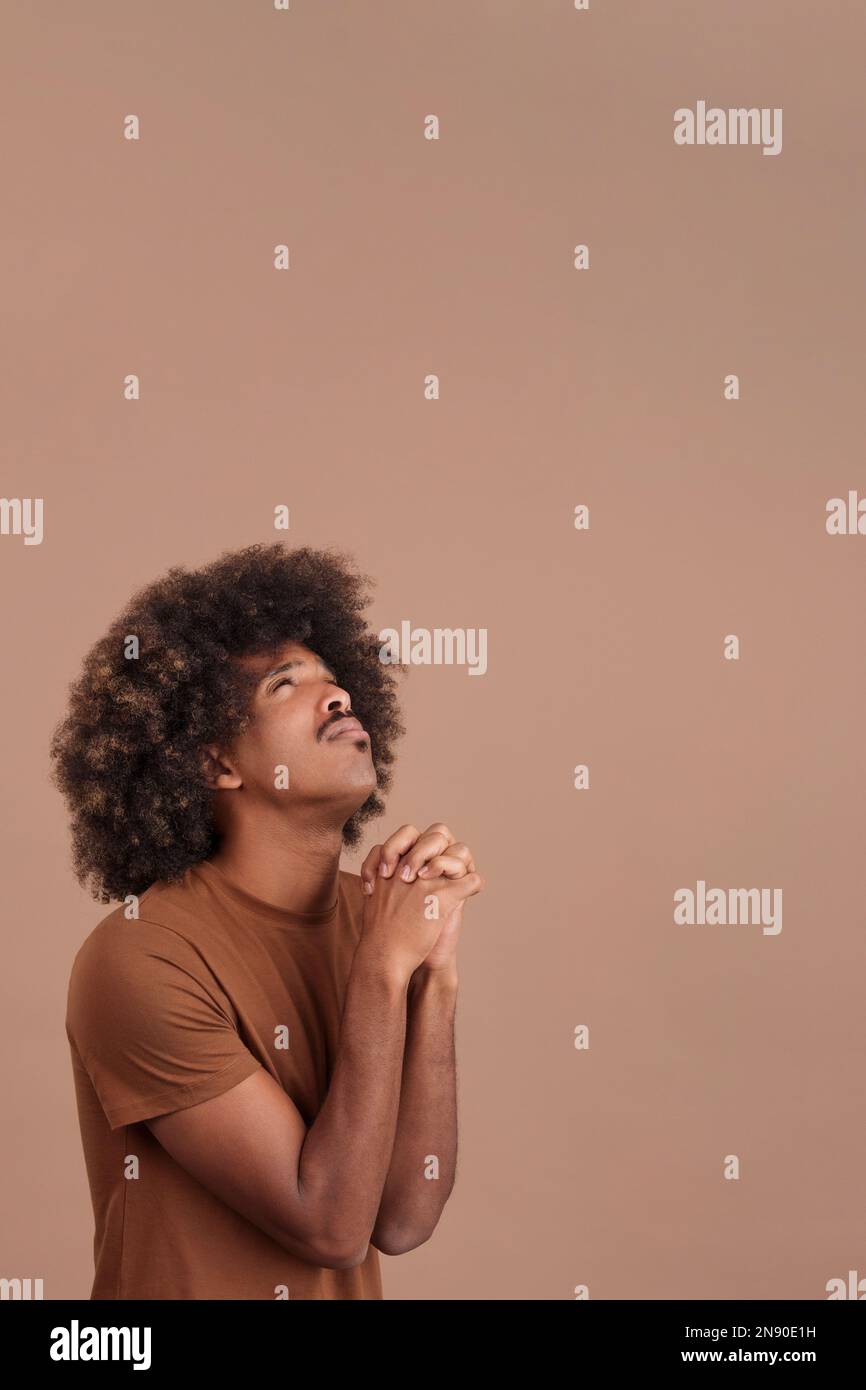 African man looking up while praying with folded hands Stock Photo