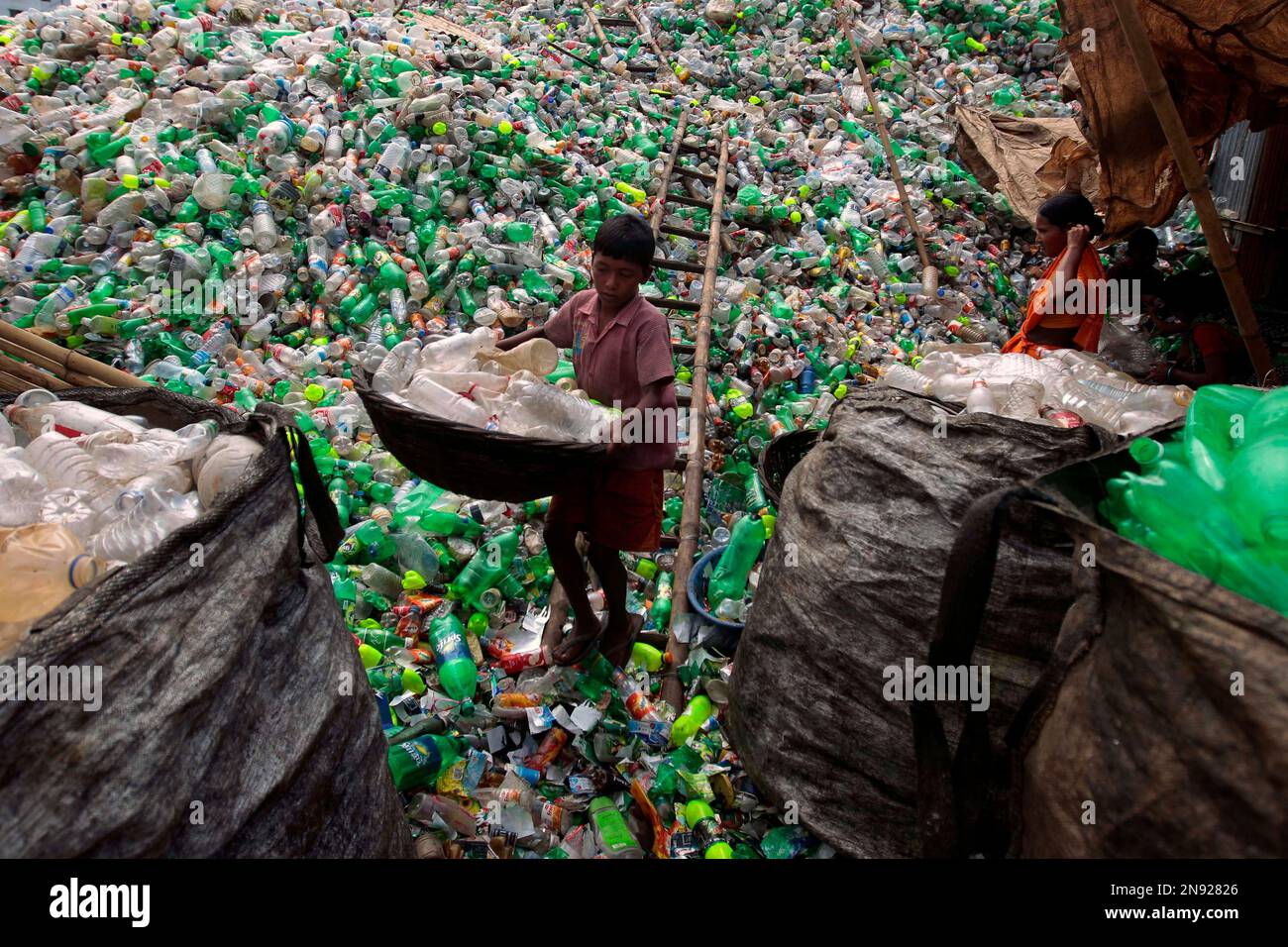 A Bangladeshi child laborer carries empty bottles at a plastic bottle recycling center in Dhaka