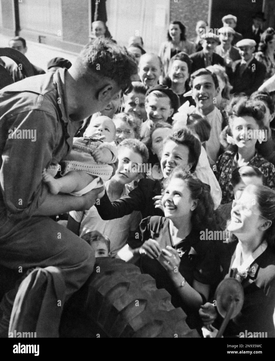 A French baby is handed up to an American Soldier by mother during ...