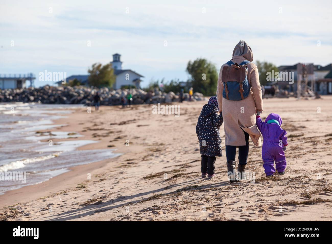 A woman with two small children walks along the beach bent over from the wind in her back Stock Photo