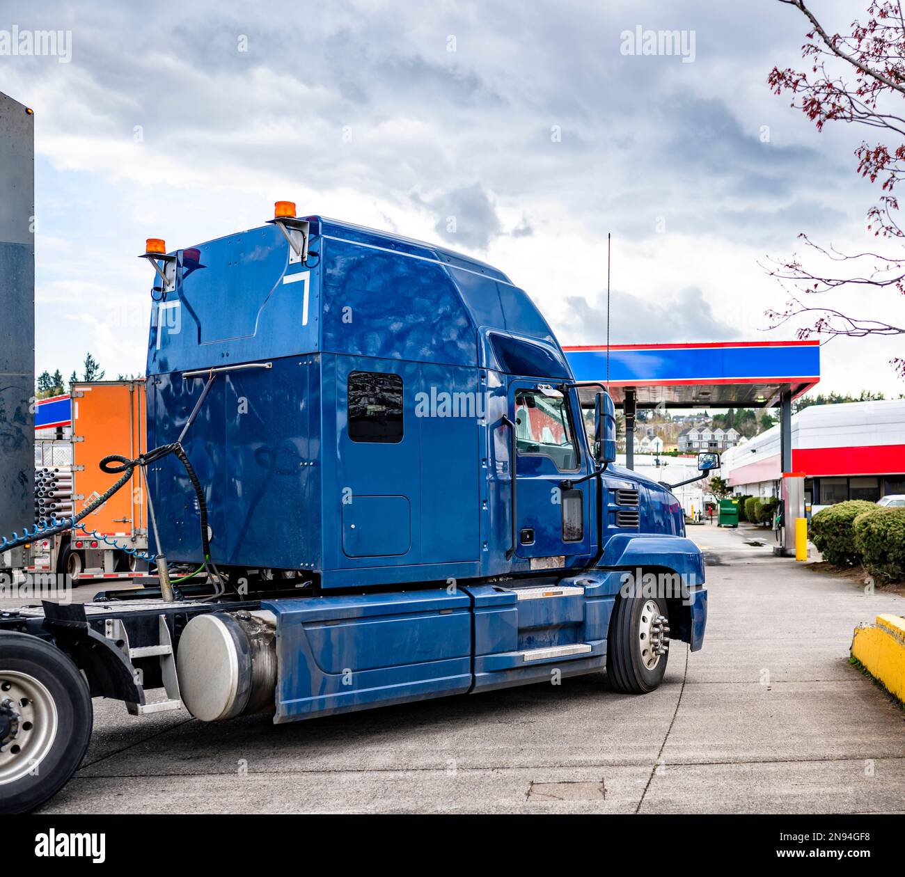 Industrial standard big rigs semi trucks with semi trailers standing on the fuel station parking