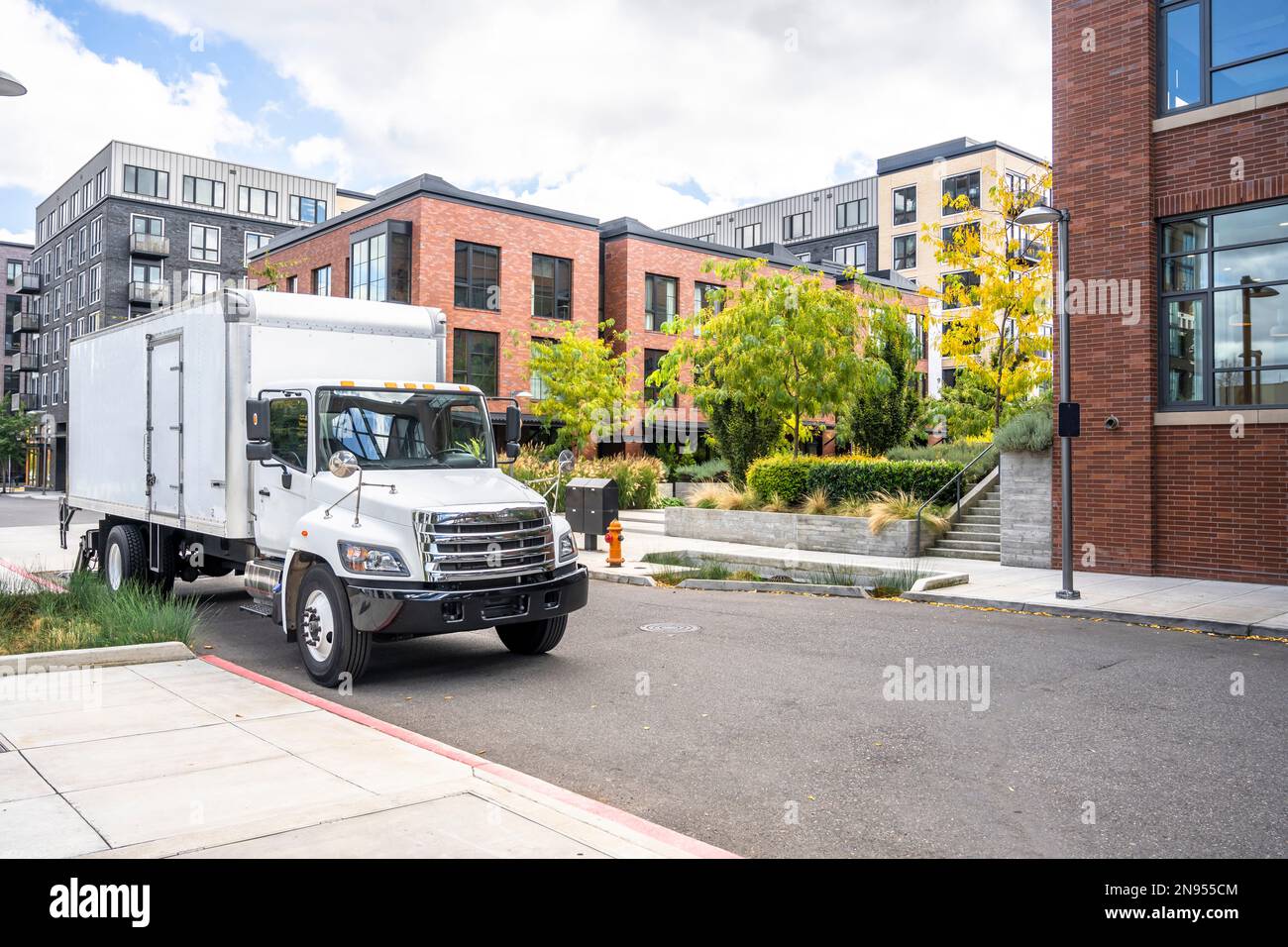 Industrial commercial compact middle duty rig white day cab semi truck tractor transporting cargo in box trailer standing on the urban city street wit Stock Photo