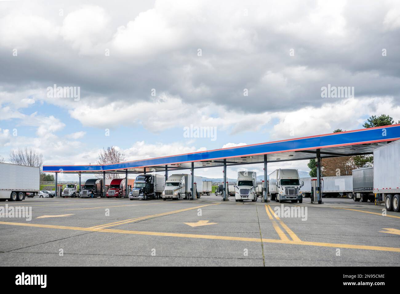 Industrial standard big rigs semi trucks with semi trailers standing on the fuel station parking