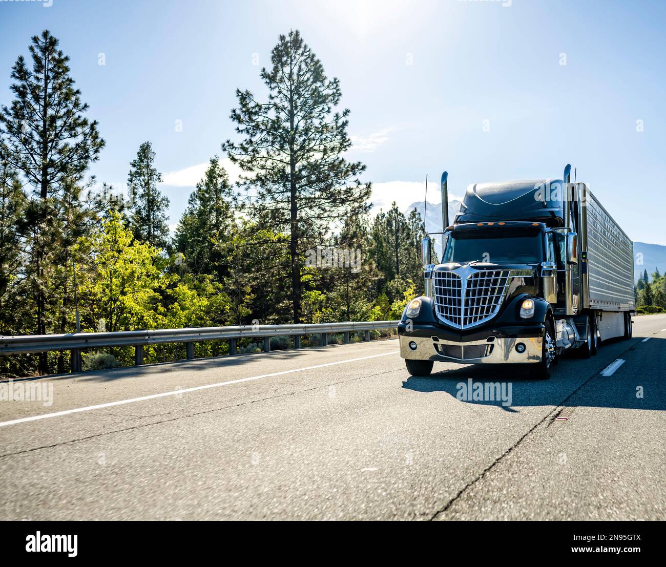 Industrial Long hauler big rig black semi truck tractor with extended cab for truck driver rest transporting frozen cargo in refrigerator semi trailer Stock Photo