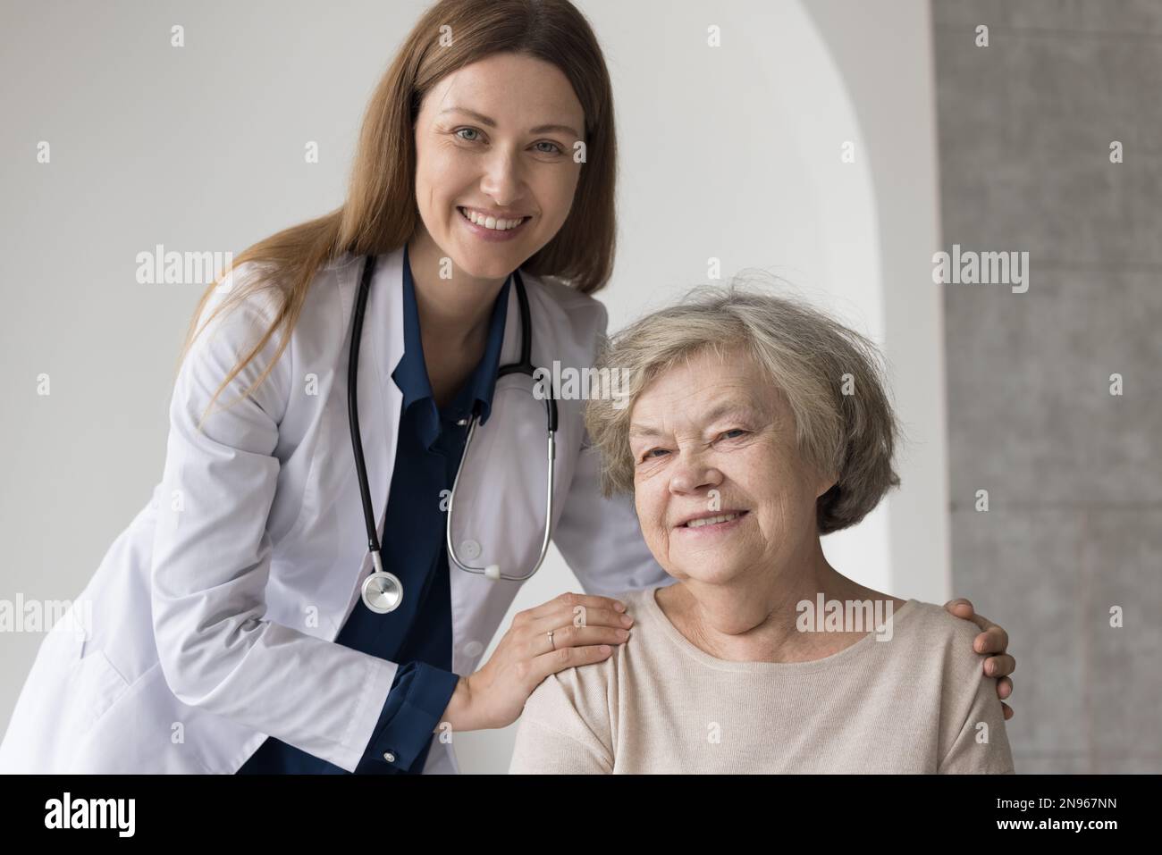 Happy pretty female doctor with stethoscope embracing older patient Stock Photo