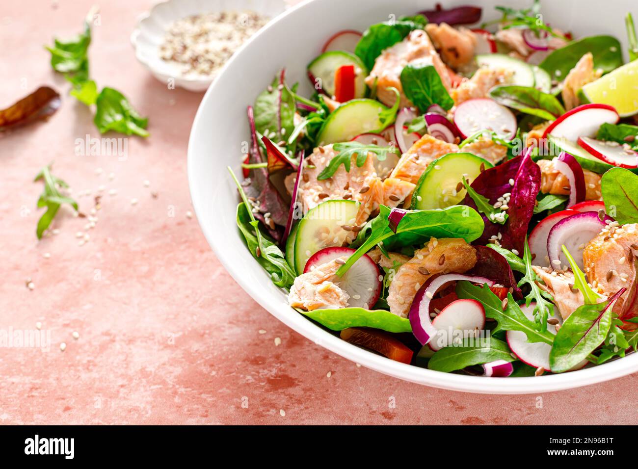 Salmon salad bowl with fresh radish, cucumber, red onion and green mixed leafy vegetables. Healthy diet food, lunch menu Stock Photo