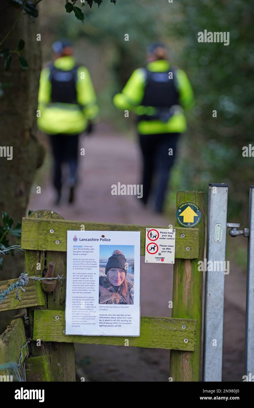 A missing person appeal poster for Nicola Bulley as police officers walk along a footpath in St Michael's on Wyre, Lancashire, as they continue their search for missing woman Nicola Bulley, 45, who was last seen on the morning of Friday January 27, when she was spotted walking her dog on a footpath by the nearby River Wyre. Picture date: Sunday February 12, 2023. Stock Photo