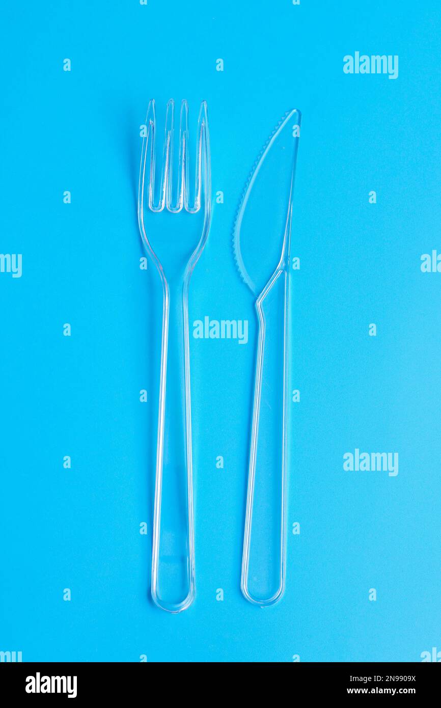 Plastic disposable tableware, cutlery. Fast food. Clean plastic fork and knive on blue background. Disposable dishes, environmental pollution. Top vie Stock Photo